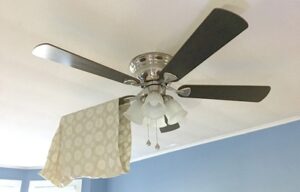 Pillowcase covering a ceiling fan blade to collect dust.