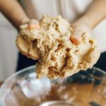 Person kneading dough in a glass bowl during a baking process at home.