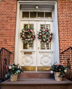 Charming New York townhouse entrance adorned with floral wreaths and potted plants.