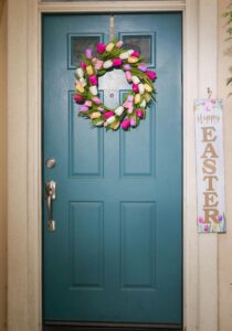 Colorful Easter wreath on a blue door with festive happy Easter sign displayed.