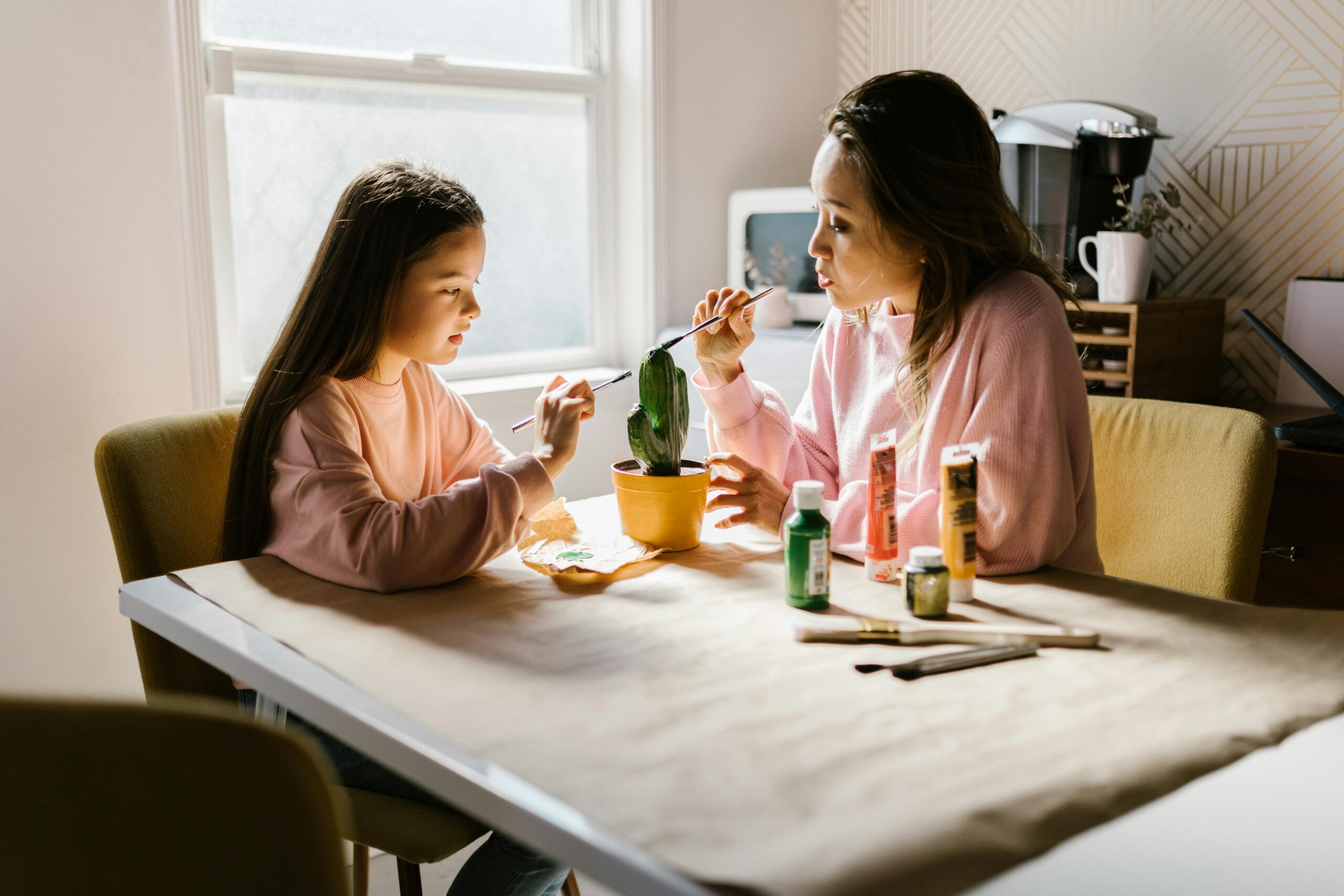 Mother and daughter enjoy painting a cactus plant together indoors under natural light.